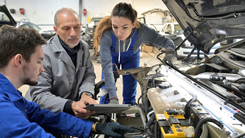 Ausbilder mit Auszubildenden bei der Arbeit an einem Auto-Motor.