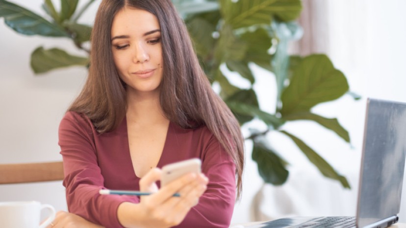 Frau an Arbeitsplatz, die auf Smartphone blickt