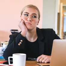 Frau in Büro blickt gelangweilt von Laptop weg