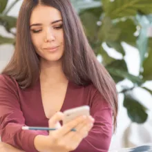 Frau an Arbeitsplatz, die auf Smartphone blickt