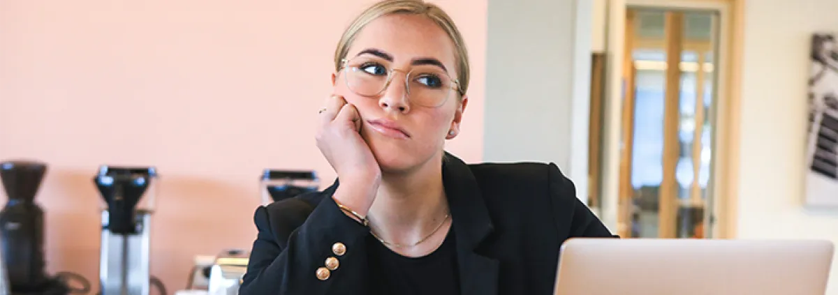 Frau in Büro blickt gelangweilt von Laptop weg