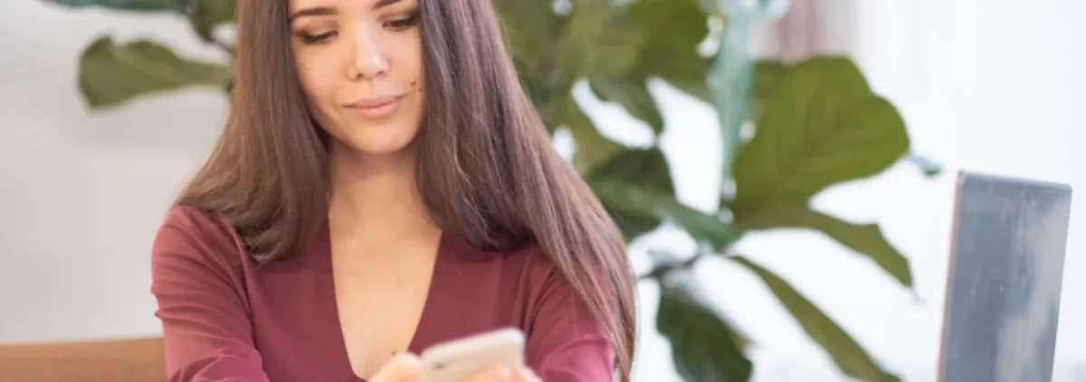 Frau an Arbeitsplatz, die auf Smartphone blickt