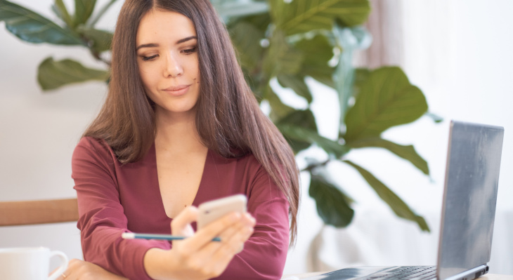 Frau an Arbeitsplatz, die auf Smartphone blickt