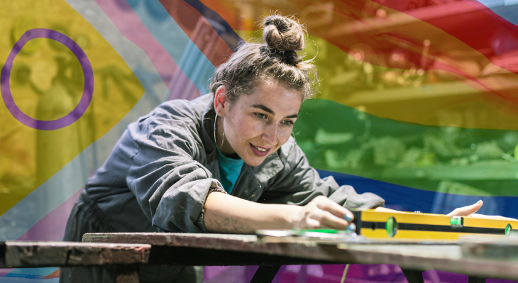 Junge Frau bei handwerklicher Arbeit vor Pride-Flagge